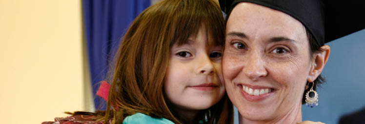 A woman wearing a cap and gown hugs a child