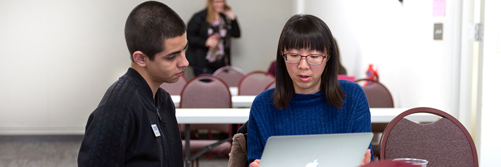 One person supervises another on a laptop