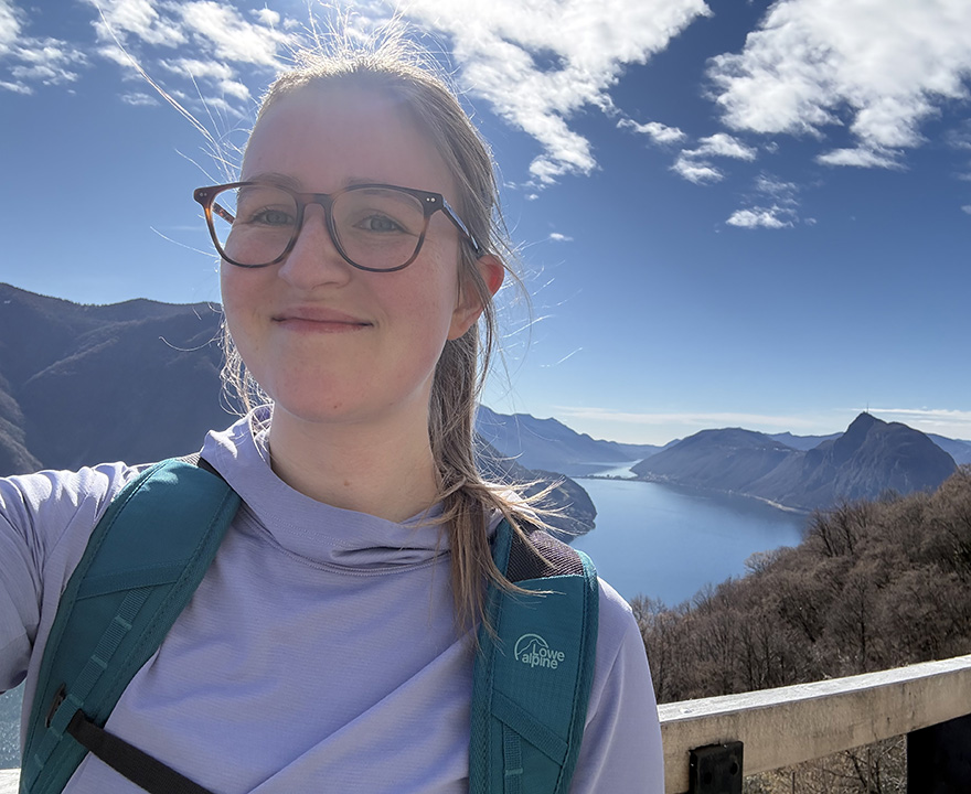 Clara Bradley taking a selfie in front of a beautiful landscape with mountains and a body of water